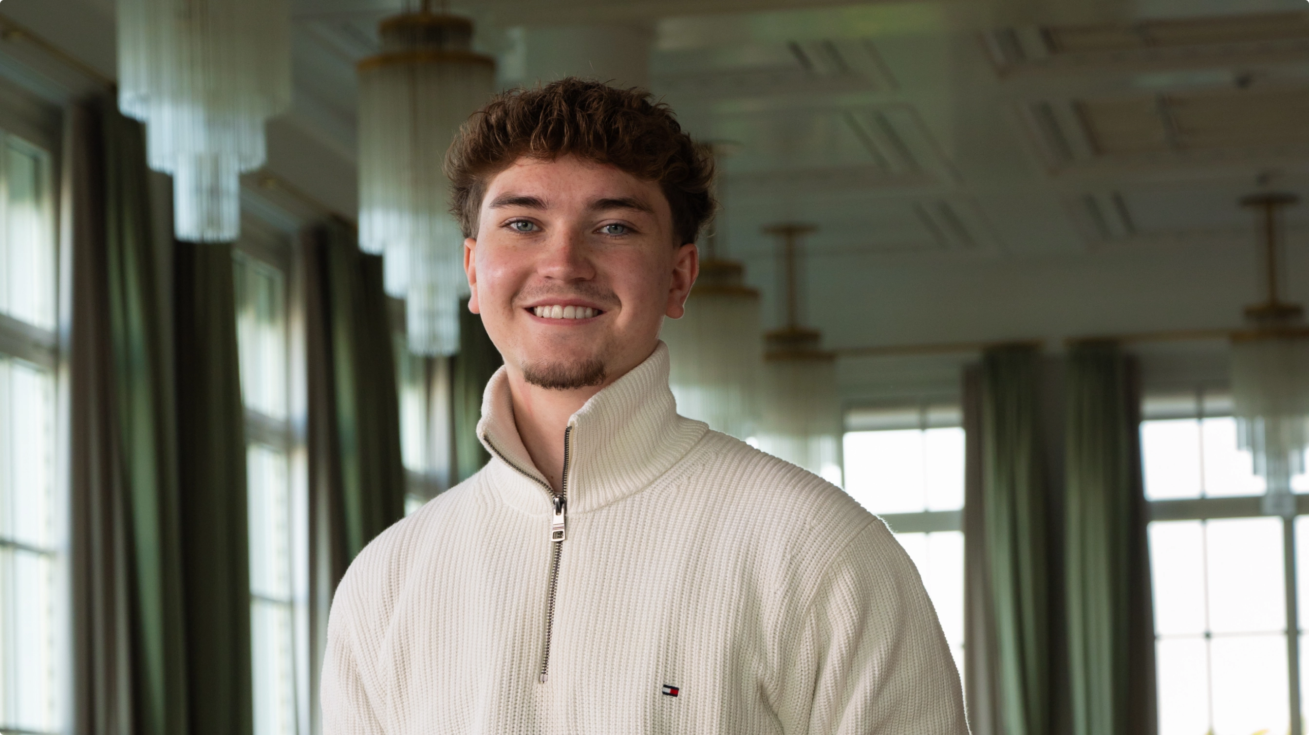 Foto von einem jungen Mann, der in einem Saal mit großen Lampen steht.